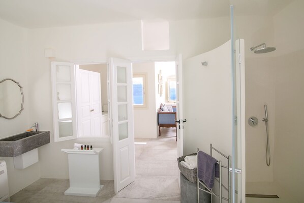 A bathroom with a shower, a sink, and a mirror. There is a door leading to another room. - My Rental Homes - Mide Suite with panoramic Jacuzzi and amazing sea view (Fira)