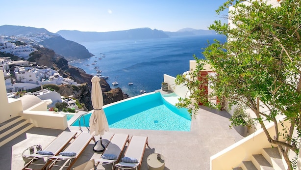 A pool area with lounge chairs and a view of the sea and distant mountains.