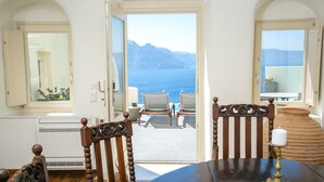 A room with a view of the sea, a dining table, and two chairs.