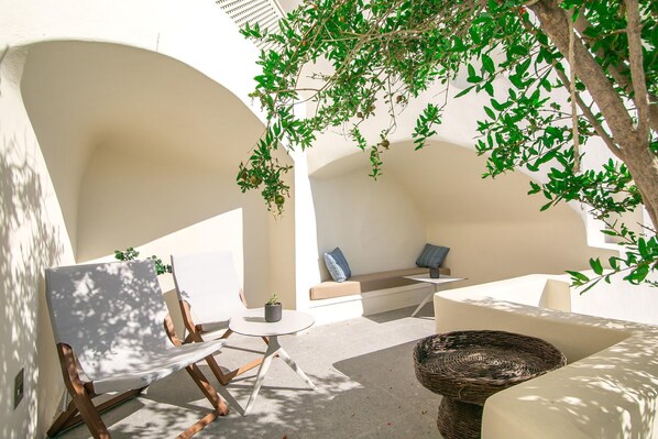 A sunlit outdoor seating area with a cushioned bench, a small round table, and a wicker chair.