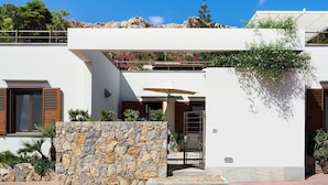Una casa moderna con parete in pietra, persiane di legno e un balcone con piante.