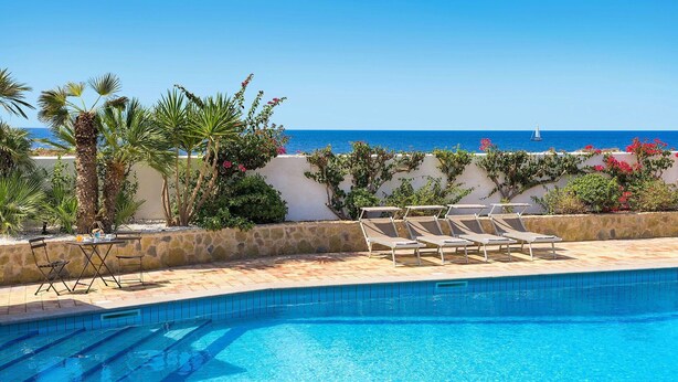 Piscina azul e límpida com espreguiçadeiras e vista para o mar.