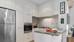 Une cuisine moderne avec des meubles blancs, des appareils en acier inoxydable et un îlot central où sont disposés des produits frais.