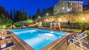 A swimming pool with lounge chairs and a gazebo, surrounded by stone walls and greenery. - My Rental Homes - Villa Monterchi with pool set in a wonderful panoramic position (Monterchi)
