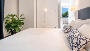 Een slaapkamer met een bed, kussens, een plant in pot en uitzicht op het landschap.