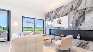 A modern living room with a fireplace, comfortable seating, and a large window offering a scenic view. - Chambre "La Garden" - Heated pool & SPA (Plaissan)
