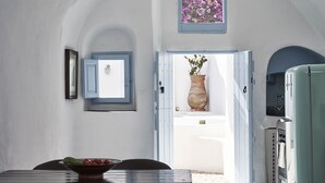 A room with a dining table, chairs, a vase with flowers, a window with a view, and a door leading outside.