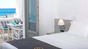 A hotel room with a bed, a nightstand with a lamp, a view of the sea through a glass door, and a seating area with chairs and a table. - Maison Ranya - My Rental Homes (Exomytis)