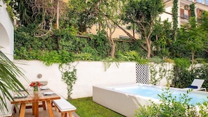 Jardí privat amb piscina, taula de fusta amb cadires i una taula petita amb un ram de flors.