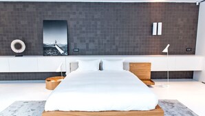 A modern bedroom with a large bed, a wooden headboard, a round bedside table, a wall-mounted lamp, and a framed picture above the bed. - My Rental Homes - Villa Sound luxury property with pool and privacy (San Jose)
