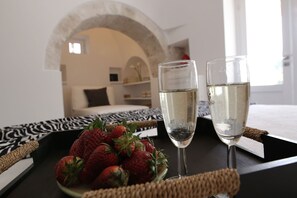Una habitación con una cama, una bandeja con fresas y dos copas de vino blanco.