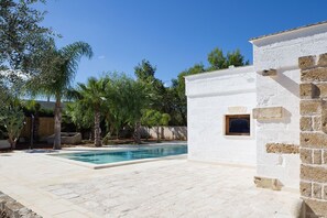 A swimming pool area with a white building, palm trees, and a stone wall. - My Rental Homes - Villa Salentina with private pool and large private garden (Cutrofiano)