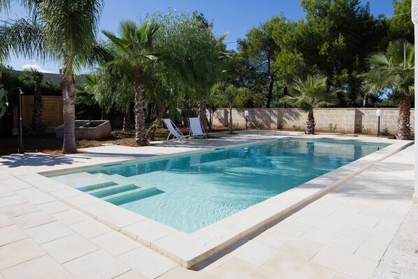 A rectangular swimming pool with clear blue water, surrounded by a tiled deck and palm trees. - My Rental Homes - Villa Salentina with private pool and large private garden (Cutrofiano)