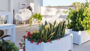 A rooftop terrace with white planters containing various plants and flowers, white chairs, and a white table. - My Rental Homes - Villa Salentina with private pool and large private garden (Cutrofiano)