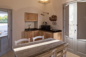 A compact kitchen with wooden cabinets, a marble countertop, and a small dining area with white chairs. - My Rental Homes - Villa Salentina with private pool and large private garden (Cutrofiano)