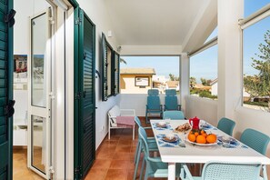 A balcony with a table set for two, chairs, and a view of the sea.