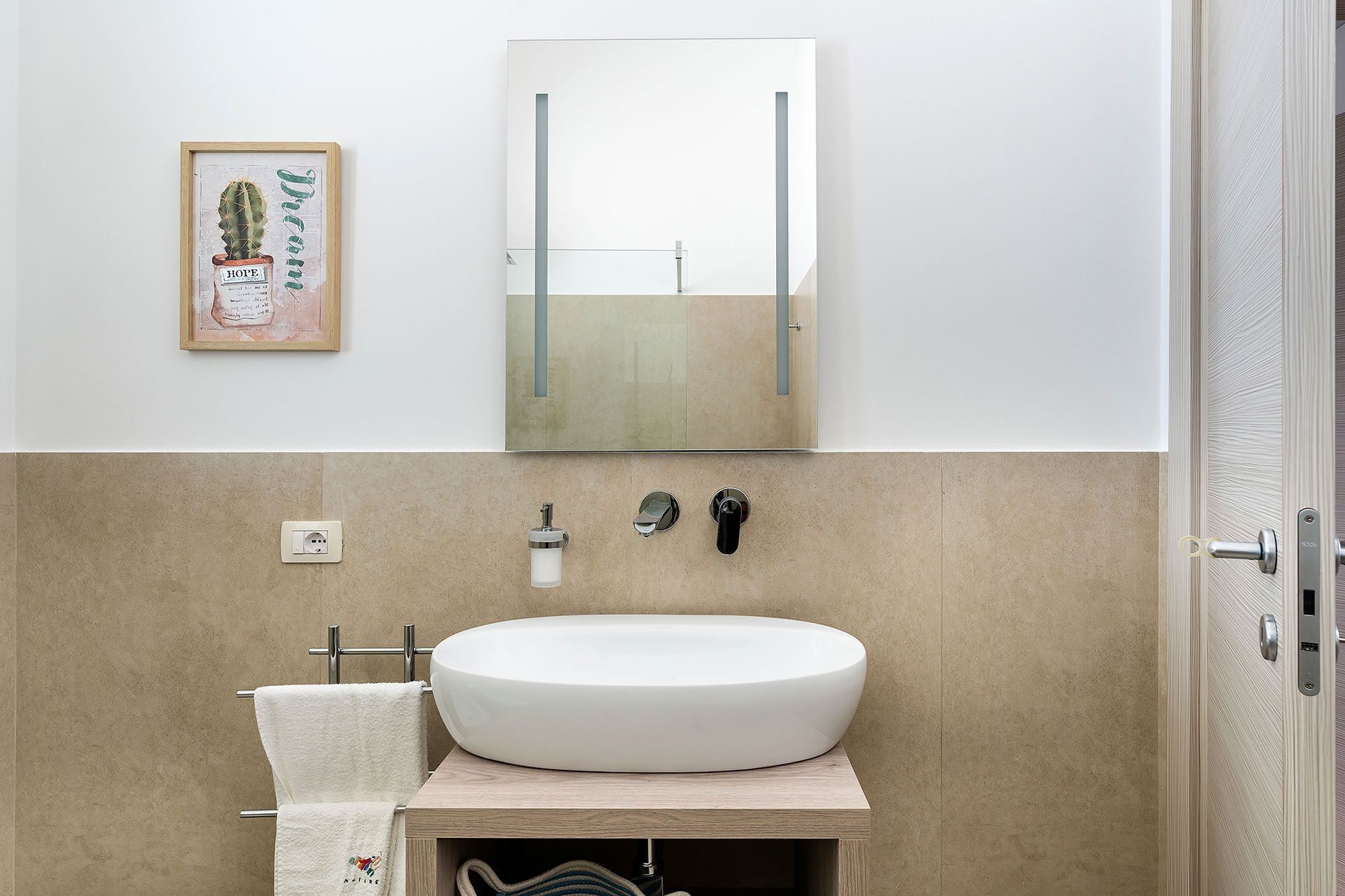 Une salle de bain avec un lavabo blanc, un miroir, une œuvre d’art représentant un cactus encadré et un porte-serviettes.