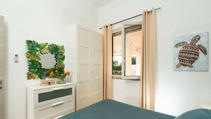 Un dormitorio con cama, cómoda, espejo, ventana con cortinas y una obra de arte en la pared.