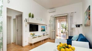 A modern living room with a TV, white furniture, a dining table with lemons, and a view to the outside. - Stella Marina near the sea  - My Rental Homes (Noto)