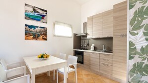A compact kitchen with a white table and chairs, a stove, and a window. - Stella Marina near the sea  - My Rental Homes (Noto)