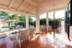 A covered patio with outdoor furniture, a dining table, and a view of the garden.