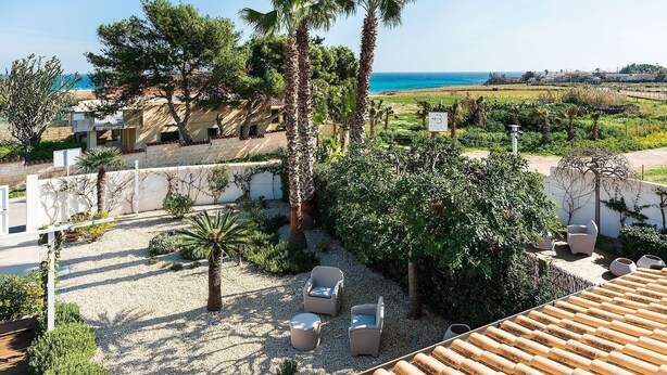 A rooftop terrace with outdoor seating, palm trees, and a view of the sea. - Stella Marina near the sea  - My Rental Homes (Noto)