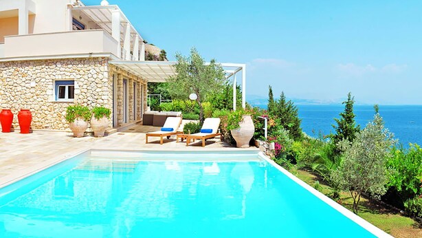 A modern villa with a swimming pool, outdoor seating, and a view of the sea.