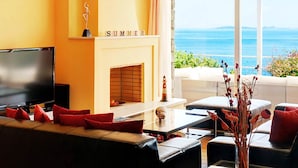 A modern living room with a fireplace, a television, and a view of the sea.