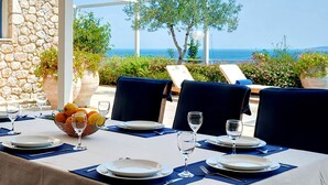 A table set for dining with a view of the sea, stone walls, and outdoor seating.