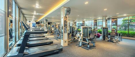 A modern gym with treadmills, weight machines, and a large window offering a view of greenery.