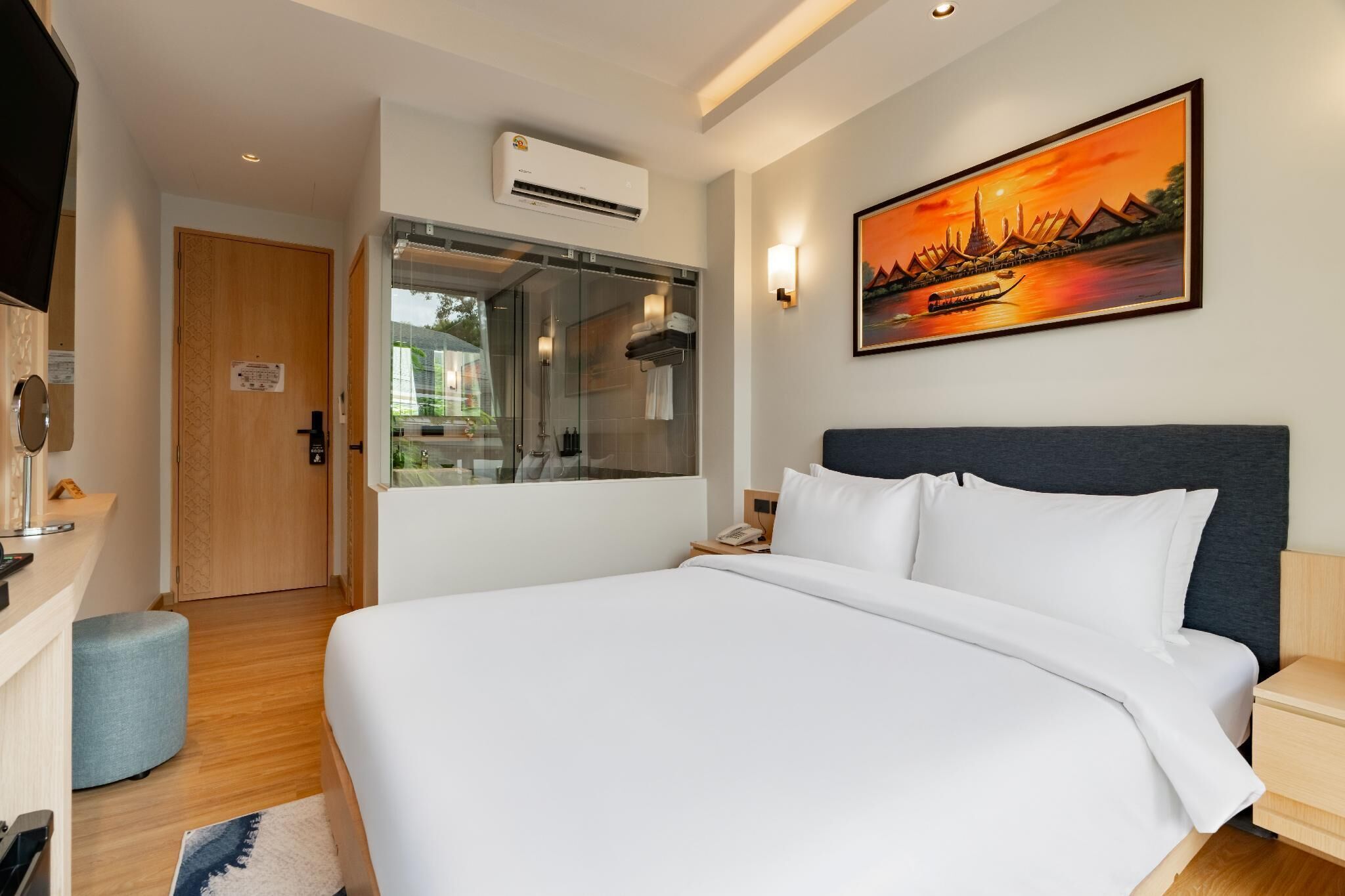 A hotel room with a bed, a TV, a shower, and a painting of a sunset.