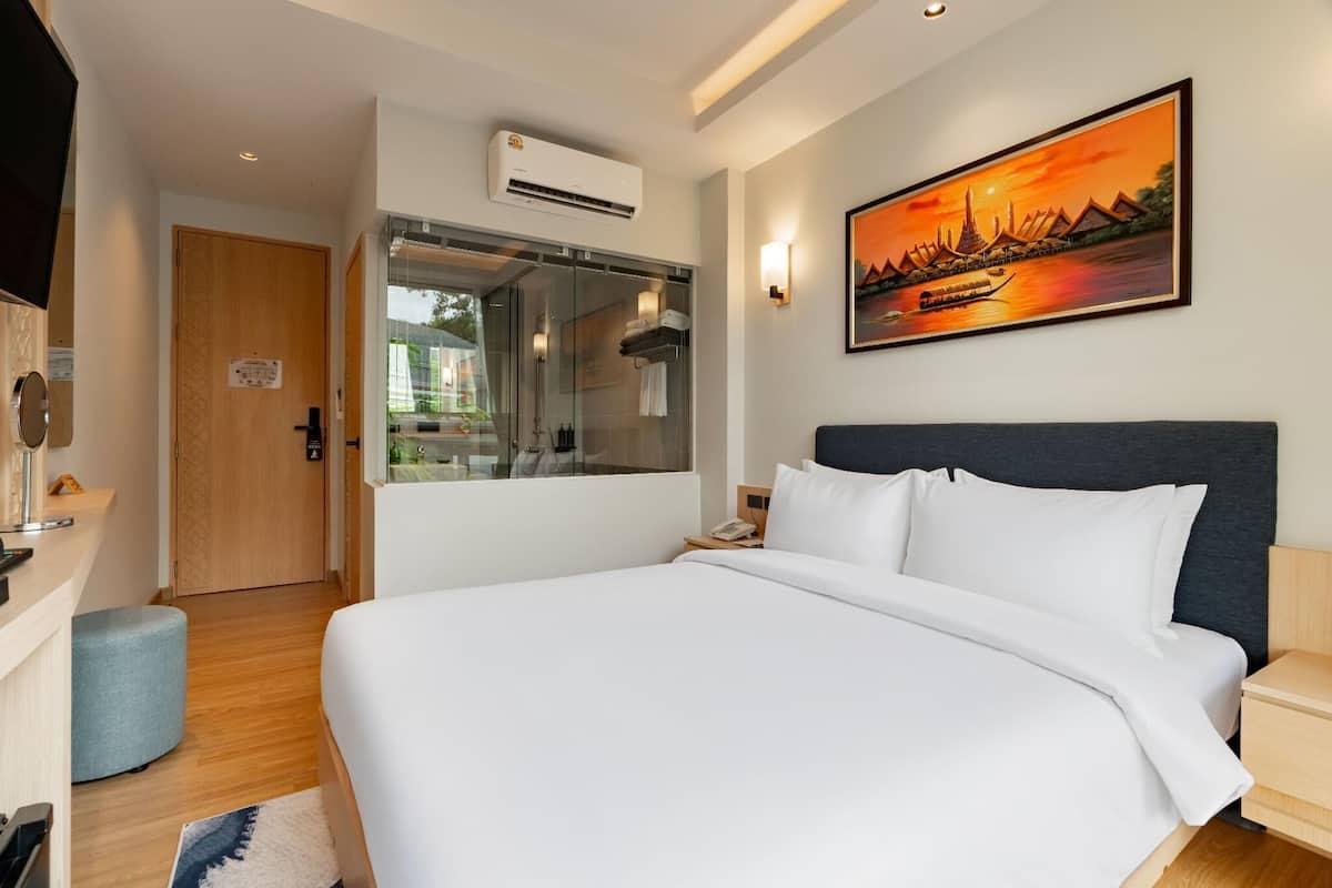A hotel room with a bed, a TV, a shower, and a painting of a sunset.