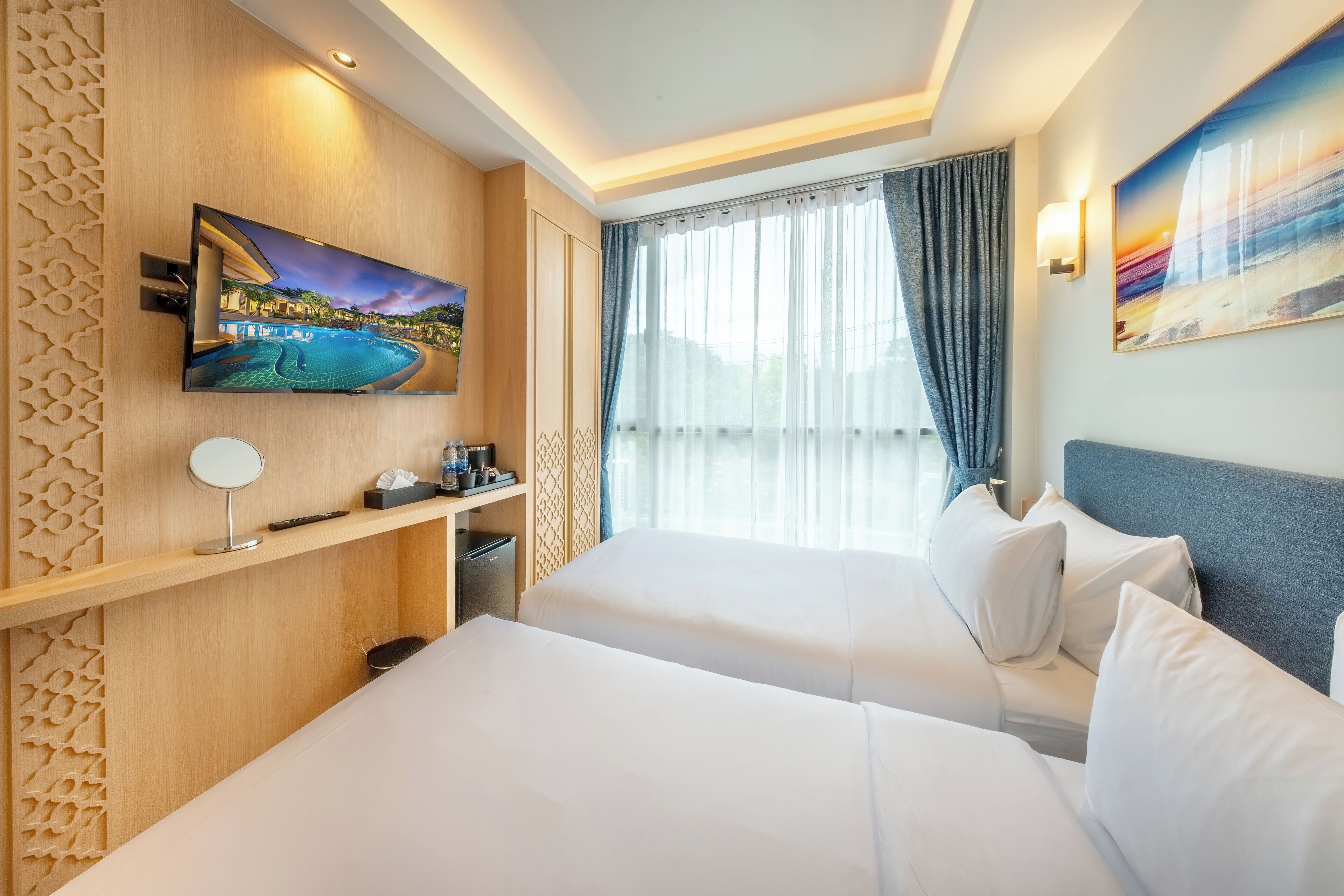 A hotel room with two beds, a TV mounted on the wall, a small desk, and a window with curtains.