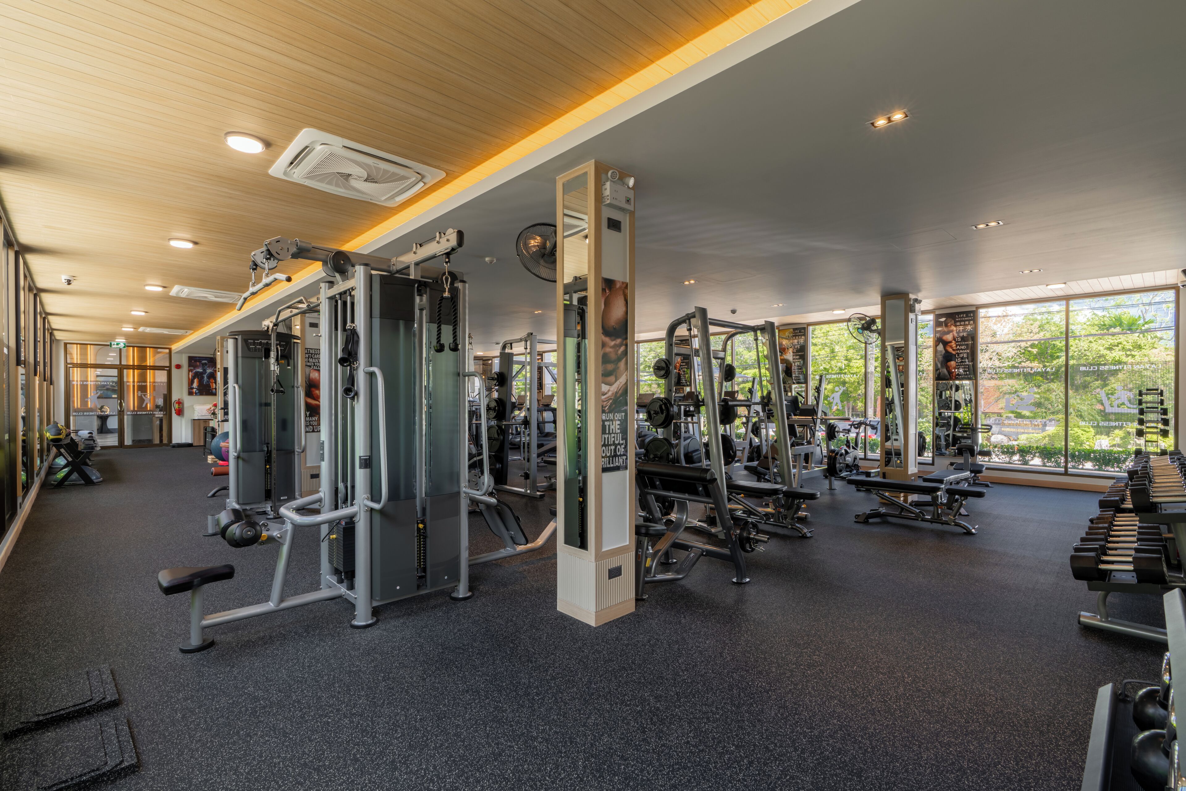 A gym with various exercise equipment, large windows, and a wooden ceiling.