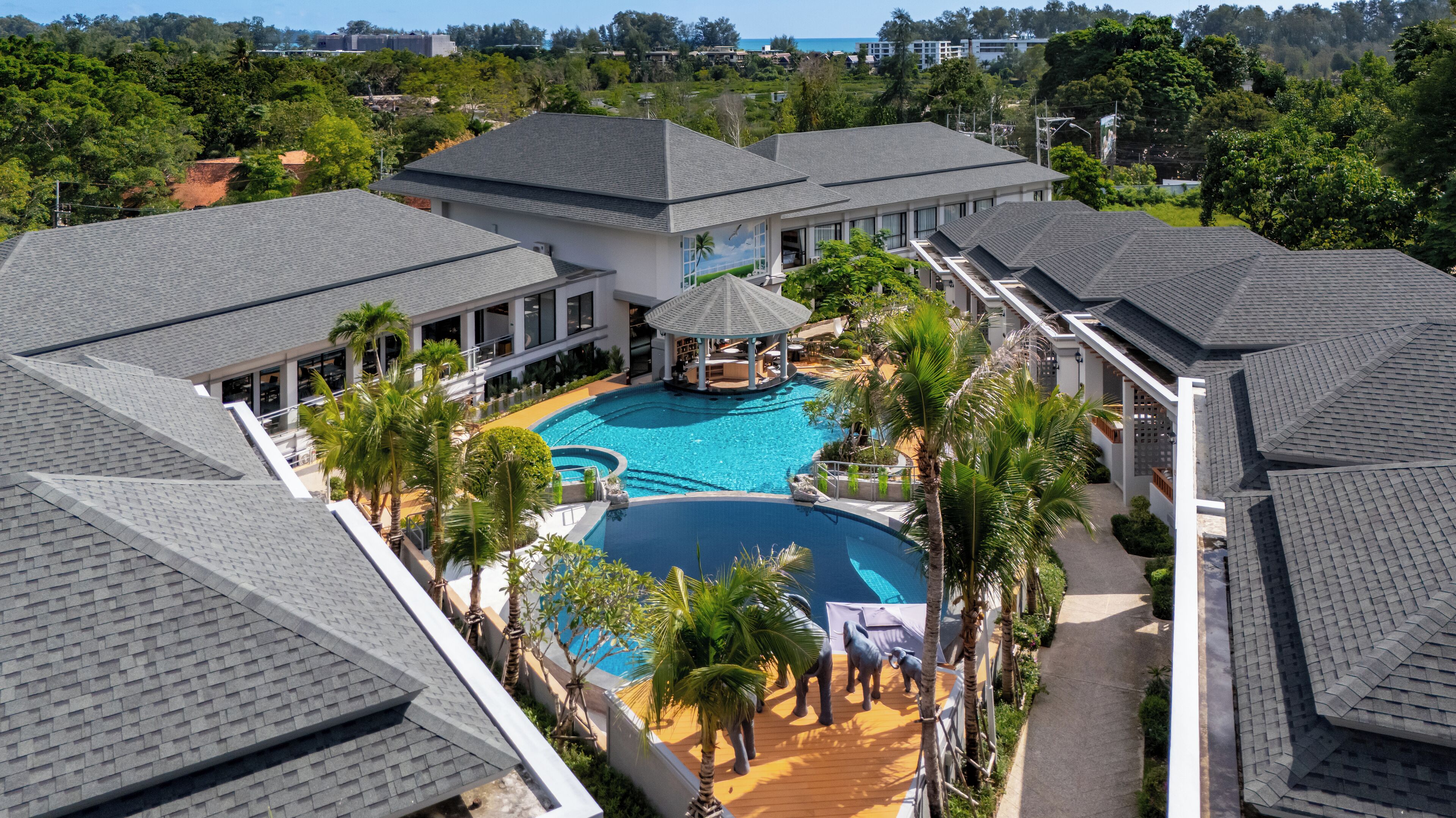 Ein Resort mit mehreren Gebäuden, einem zentralen Schwimmbad und Palmen.