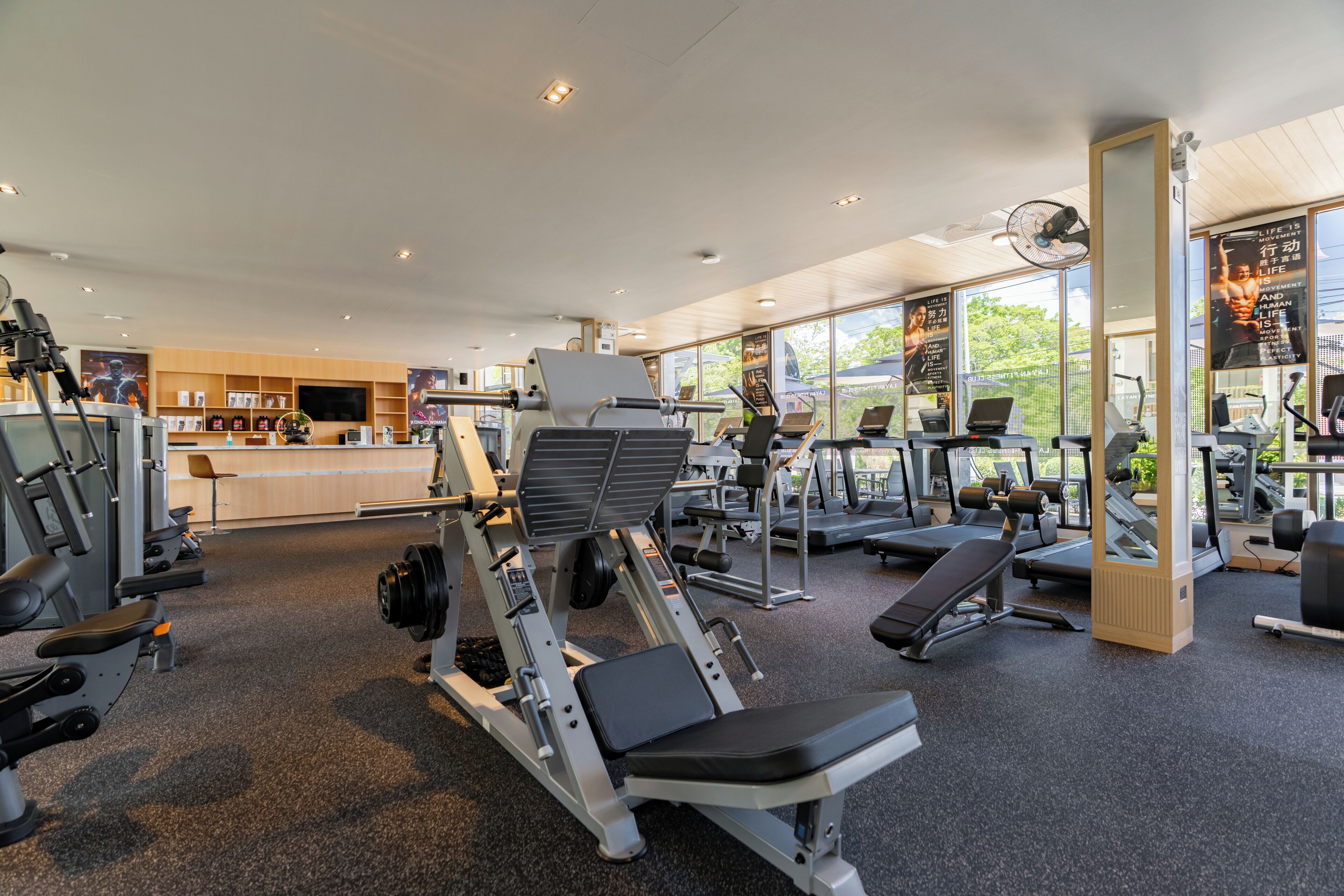 Uma academia moderna com diversos equipamentos de exercício, uma área de recepção e grandes janelas que proporcionam luz natural.