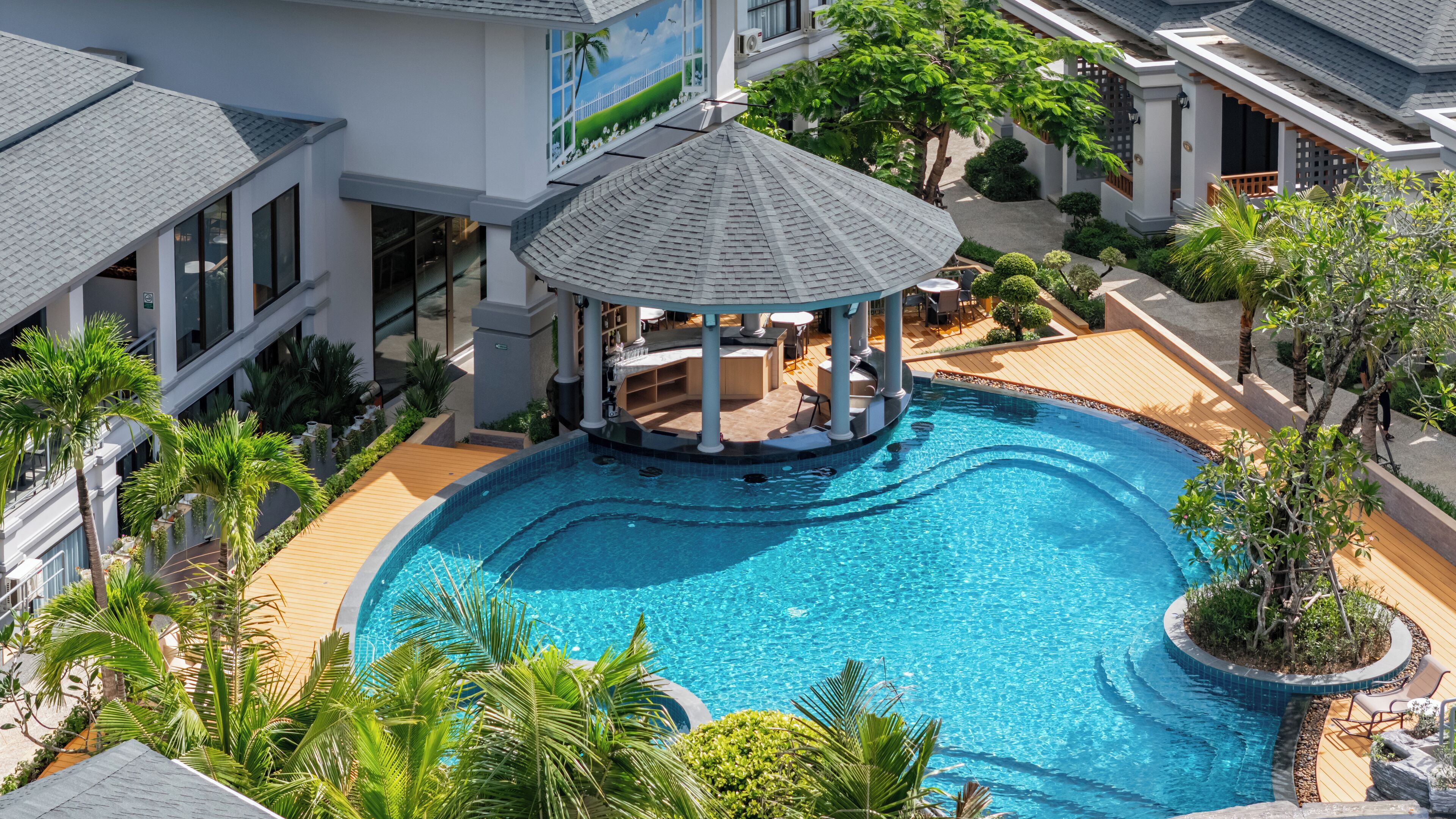 A large, clear swimming pool with a gazebo in the center, surrounded by lush greenery and modern architecture.