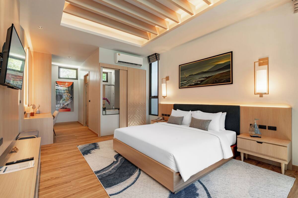 A modern hotel room with a large bed, bedside tables, a flat-screen TV, and a painting on the wall.