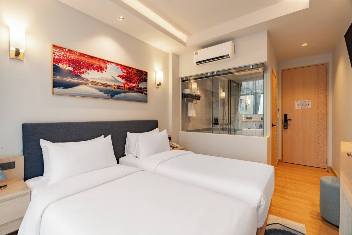 A hotel room with a large bed, a bathroom with a glass shower, and a painting on the wall.