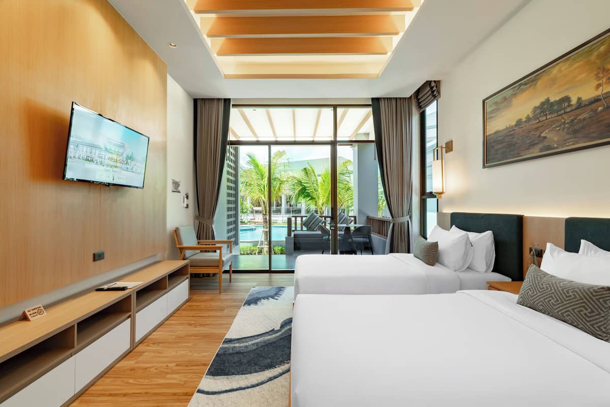A modern hotel room with a large bed, a TV mounted on the wall, a desk, and a view of the pool and palm trees.