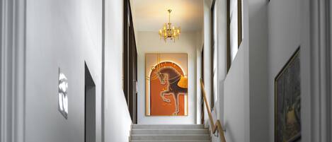 Una escalera con barandilla de madera, un candelabro y una obra de arte enmarcada en la pared.