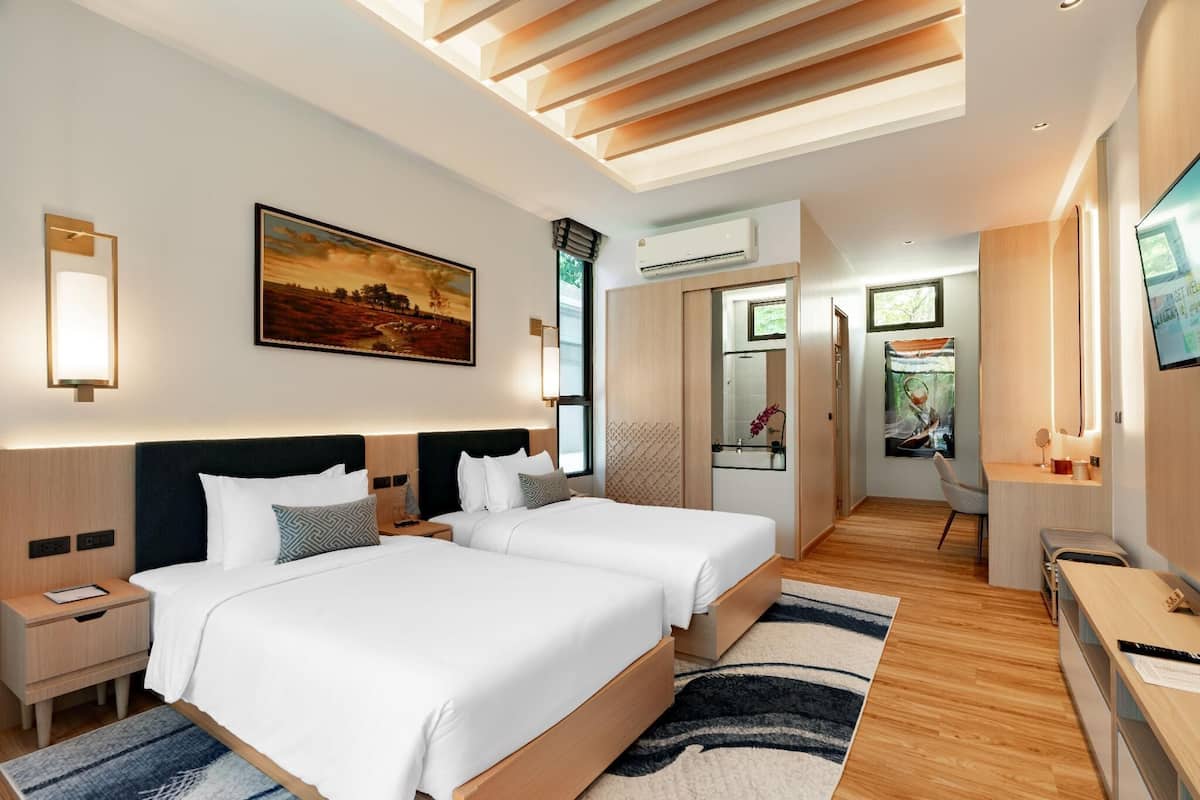 A modern hotel room with two beds, a desk, a TV, and a painting on the wall.