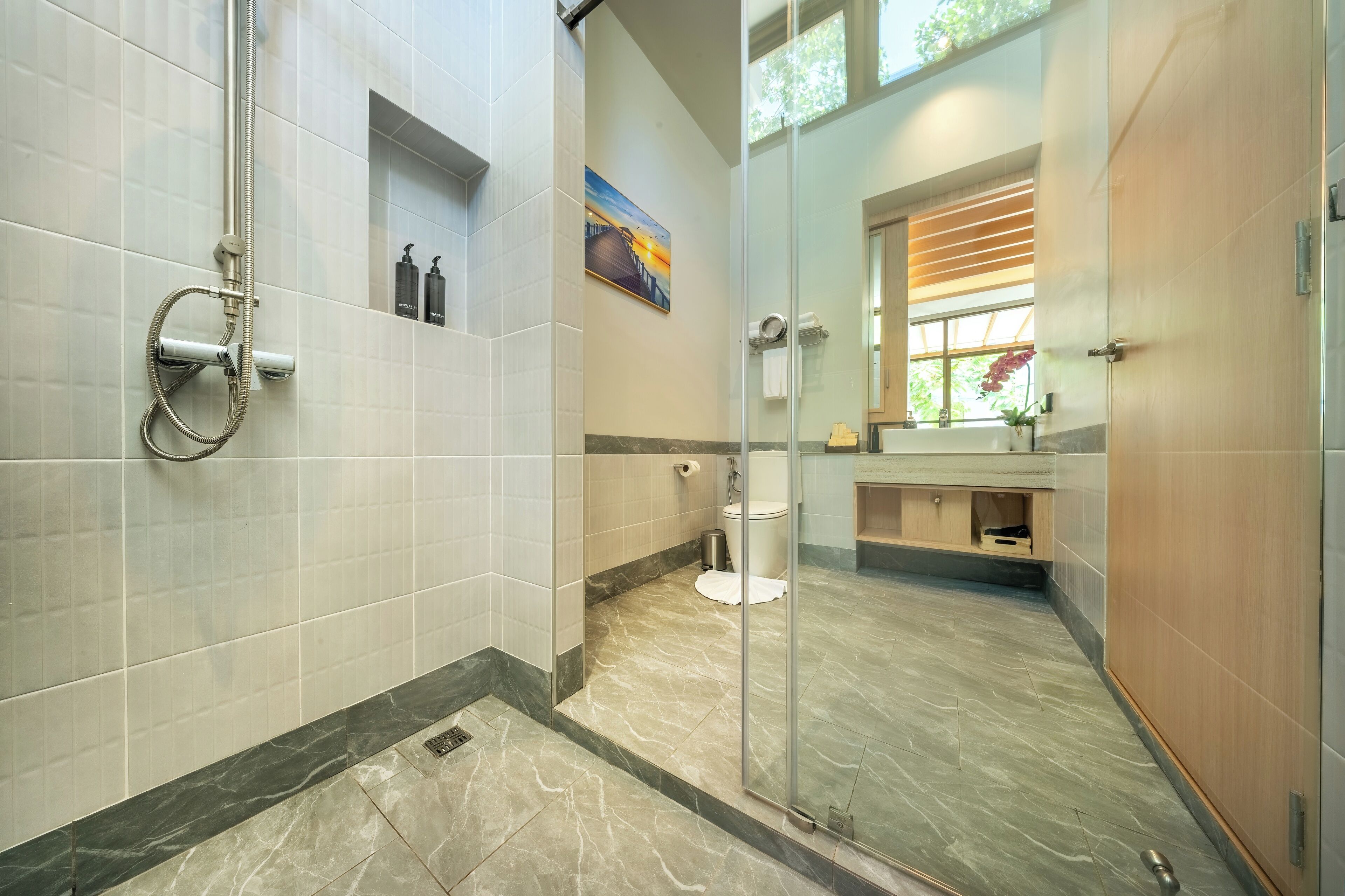 Une salle de bain moderne avec une douche à l’italienne en verre, un sol en marbre et un grand miroir.