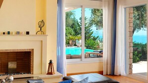 Un salon doté d’une cheminée, donnant sur la piscine et agrémenté d’un mur en pierre.