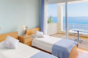 A hotel room with two beds, a nightstand, a lamp, and a view of the sea. - Villa Azzurra with private pool - My Rental Homes (Corfu)