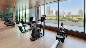 Ginásio com máquinas de cardio e amplas janelas com vista para a cidade.