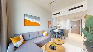 Uma sala moderna com um sofá cinzento, duas mesas redondas de madeira e uma área de cozinha ao fundo.