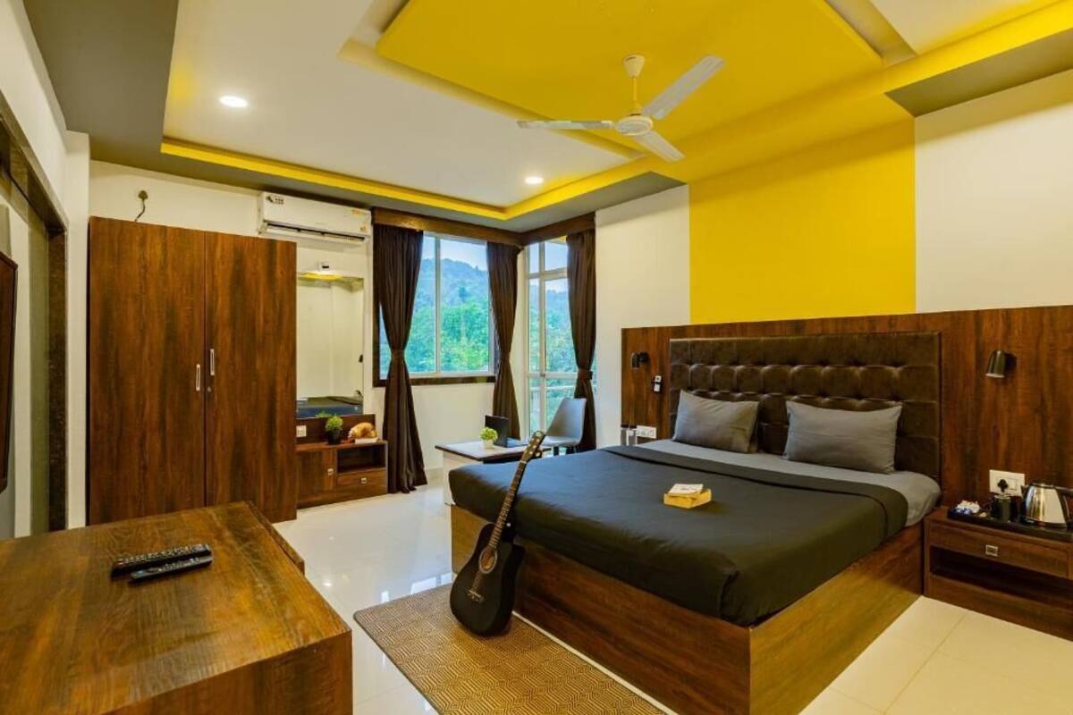 Een slaapkamer met een groot bed, een houten garderobe, een bureau en een gitaar.