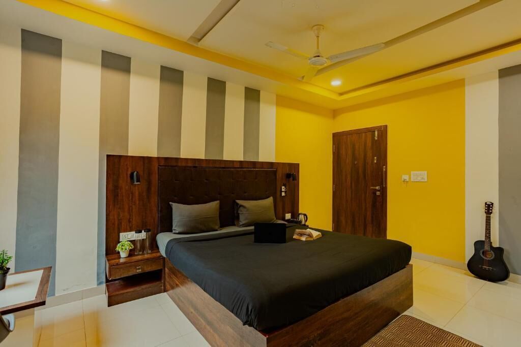 A bedroom with a large bed, a wooden headboard, a guitar, and a nightstand with a lamp.