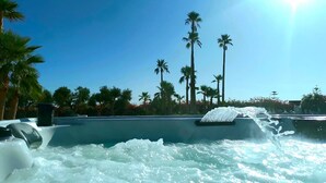 Ein Whirlpool mit Wasserstrahlen, umgeben von Palmen und blauem Himmel.